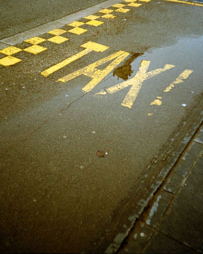 A wet city street highlighting yellow taxi lane markings with reflections in puddles.